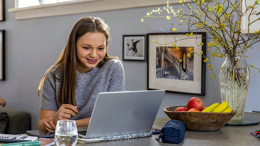 Glad ungdomsskoleelev sitter i sengen med sin laptop og får hjelp til matematikk online
