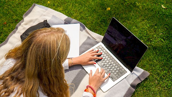 Videregåendeelev sitter med sin laptop i parken og får hjelp i norsk