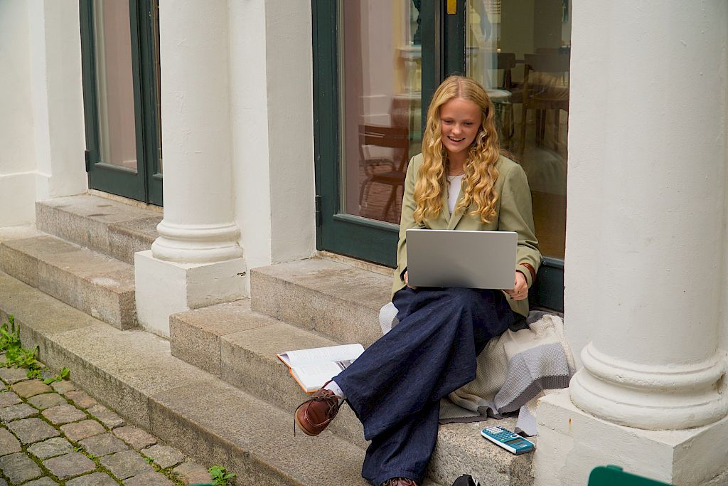 Elev smiler glad i nettundervisning fram mot eksamen mens hun sitter utendørs.