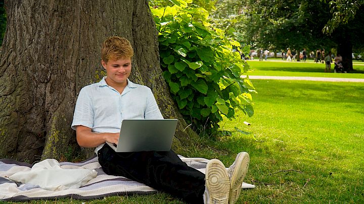 Elev sitter utendørs og har nettundervisning.