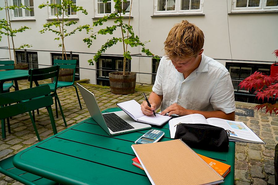 Elev skriver notater mens han får nettundervisning.