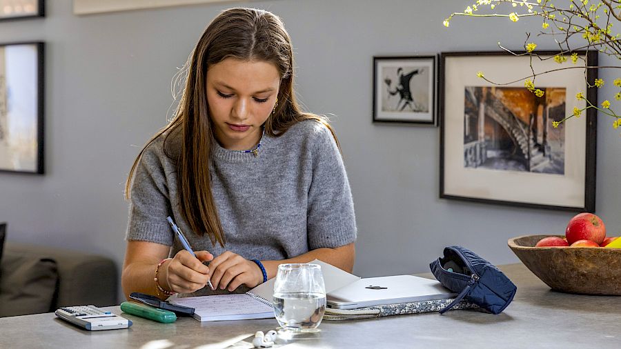 Elev skriver ned notater mens hun får nettundervisning.