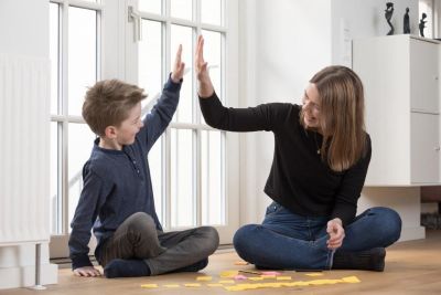 Barn og voksen sitter på gulvet og gir high-five