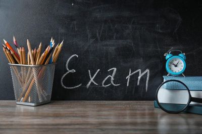 Tavle med skriften "Exam" og en blyantholder, klokke og forstørrelsesglass