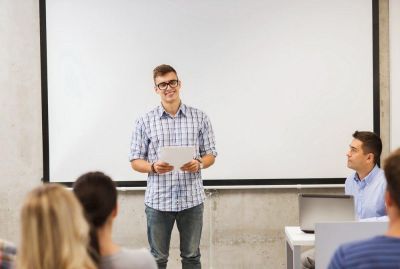 Lærer som står foran en tavle i klasserommet mens elever ser opp på ham