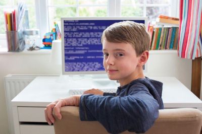 Gutt sitter ved skrivebord og ser på en skjerm med kode