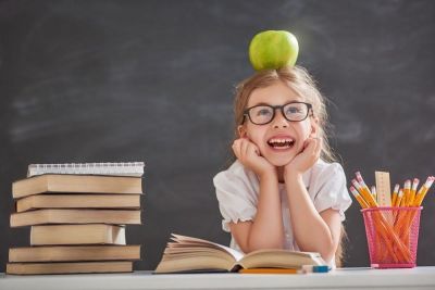Glad barneskoleelev sitter med eple på hodet ved et skrivebord