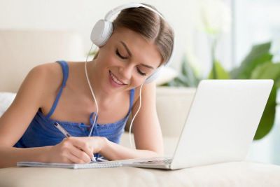 Glad student jobber foran datamaskinen med musikk i ørene